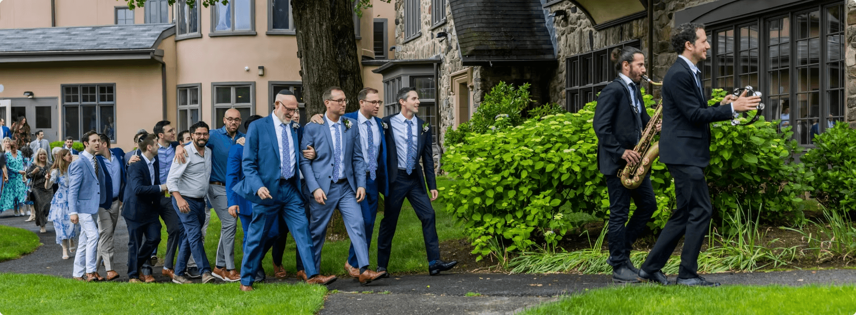 Two horn players leading a groom and his guests across a lawn