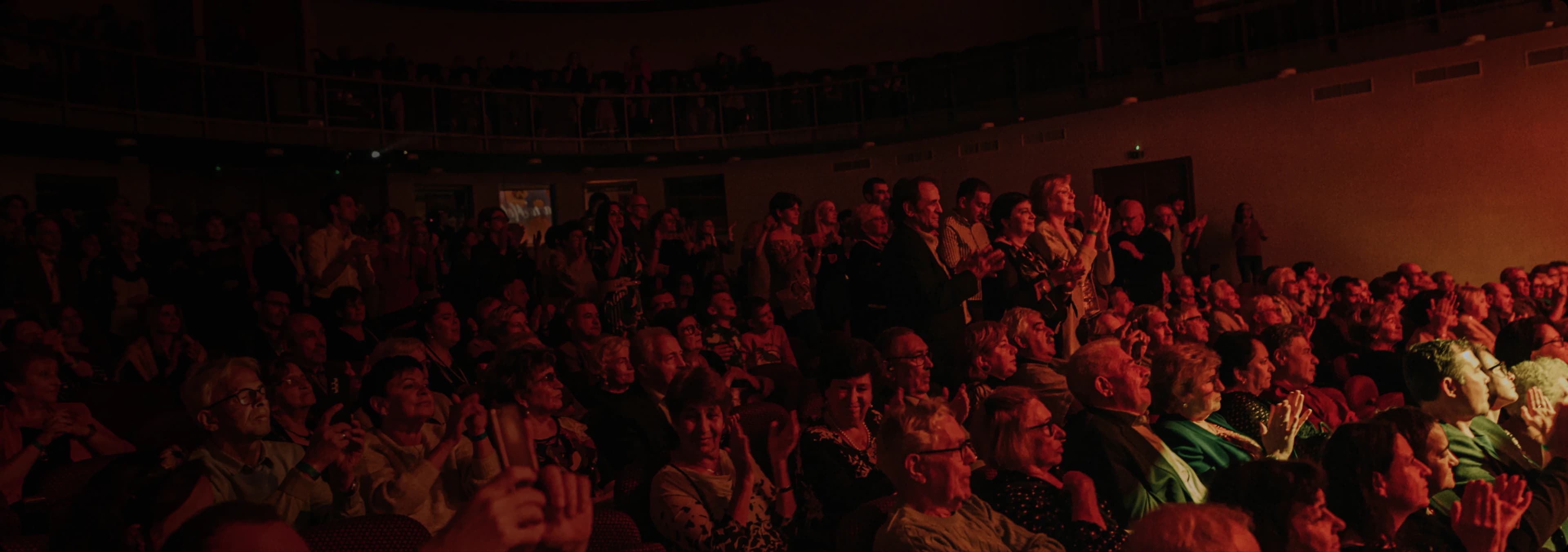 A packed theatre audience watching a performance under warm amber light