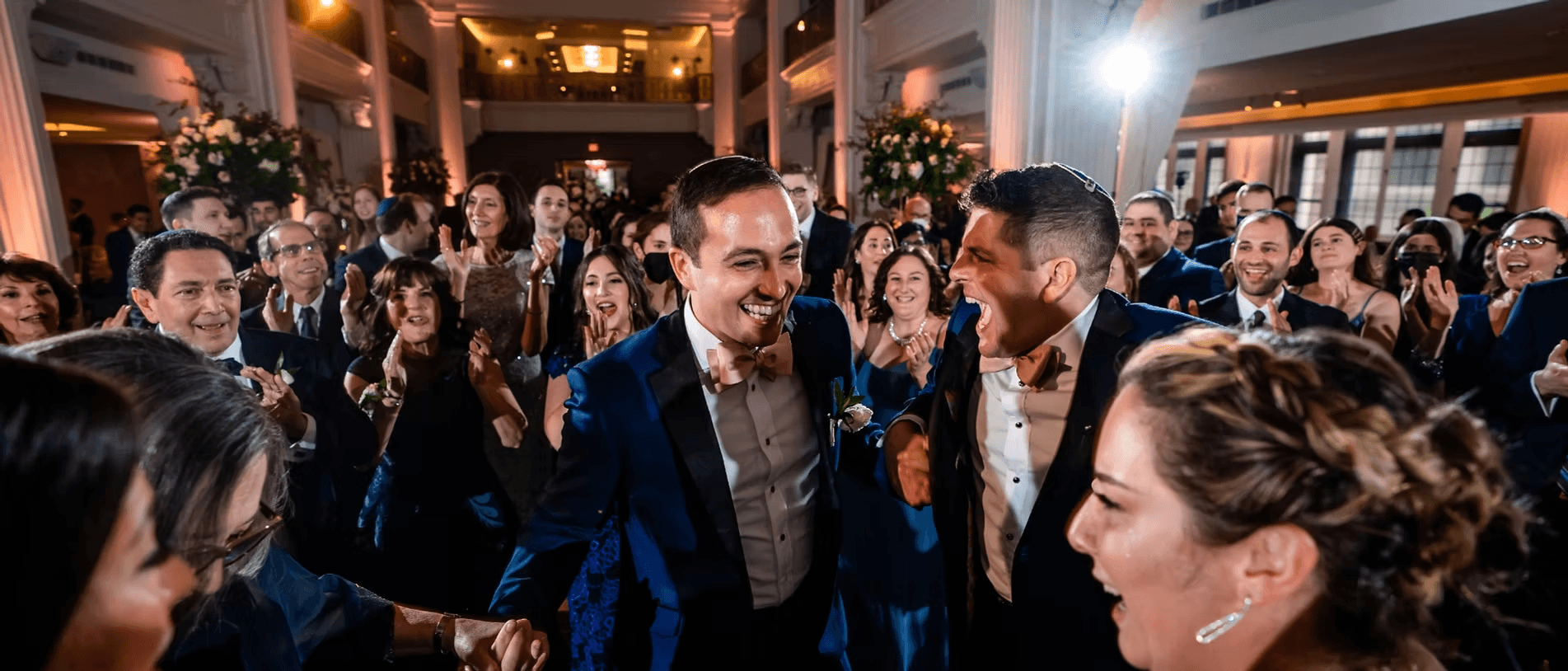 Two men in black tie celebrating together, surrounded by cheering guests in a ballroom