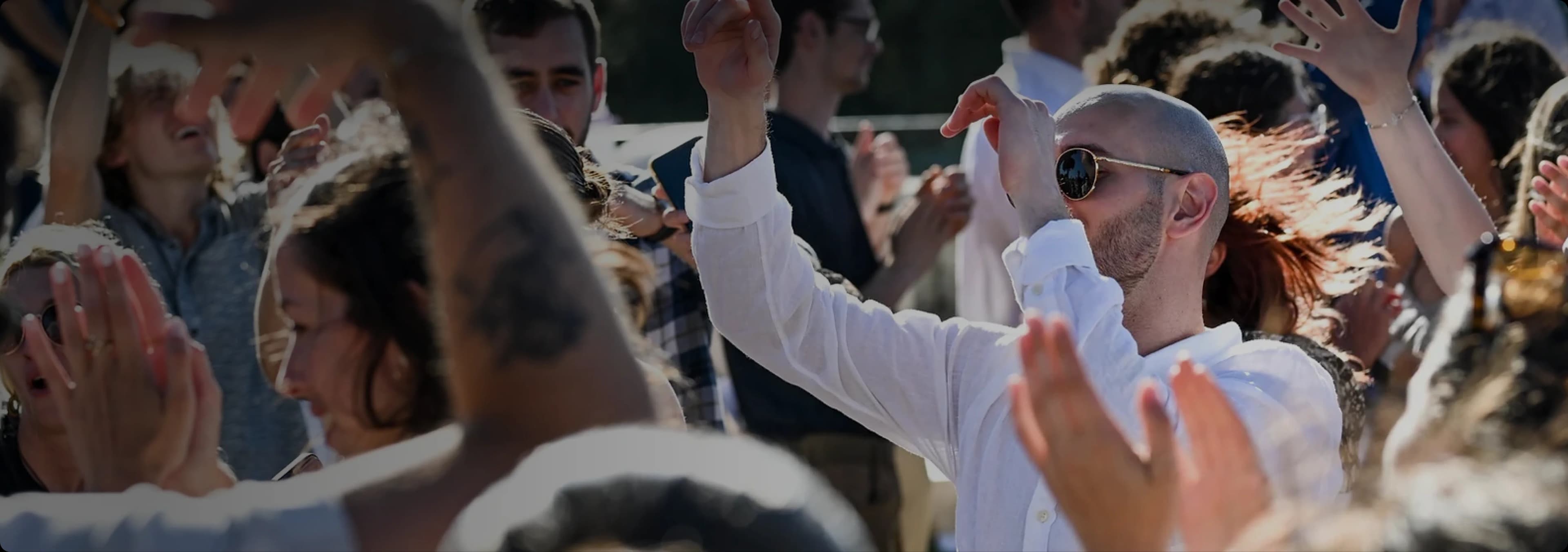 Guests outdoors in bright sunshine, hands raised and clapping along to the music