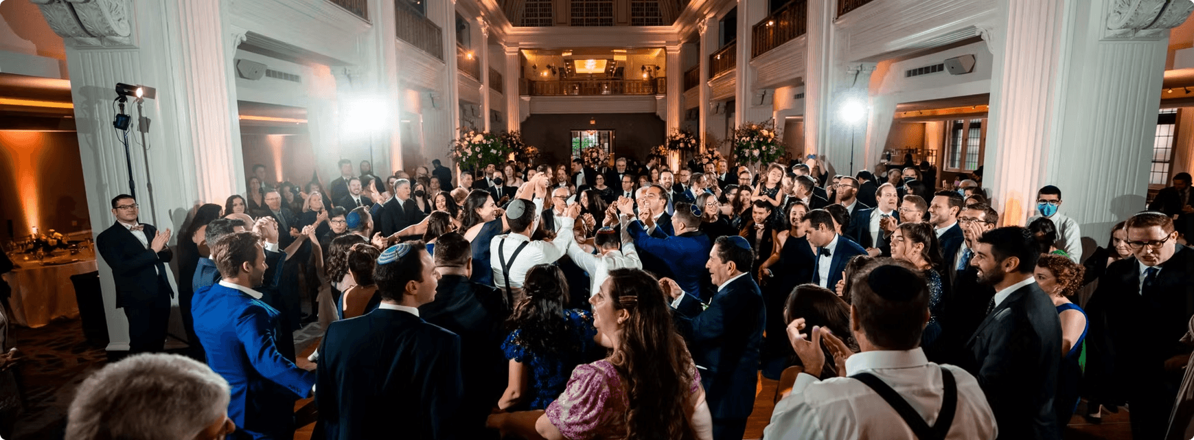 A crowded dance floor at an evening celebration in a pillared ballroom